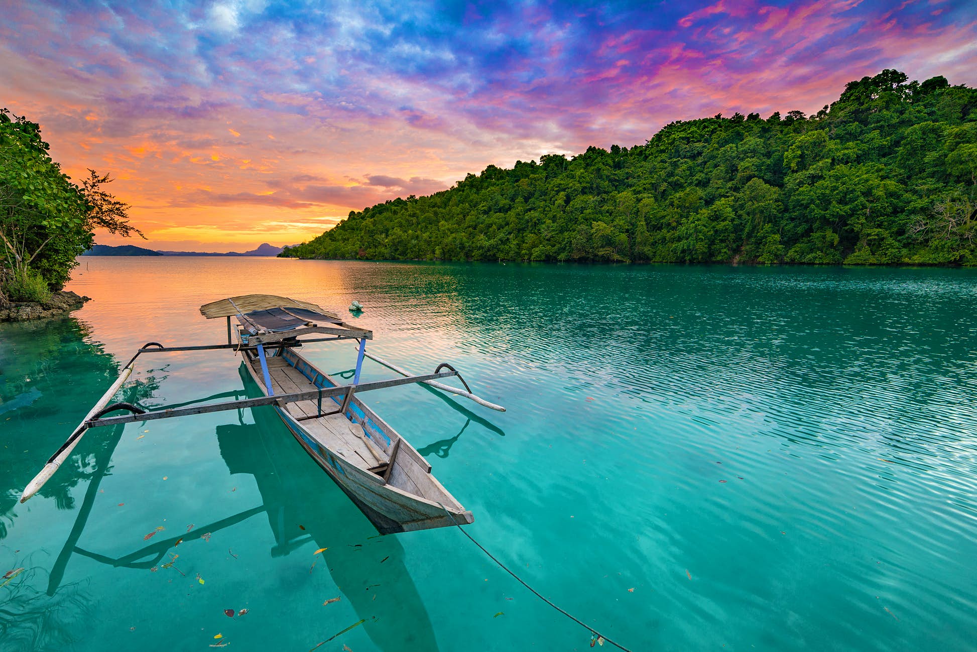 A small boat on still water during sunset at the Togian Islands. ©Fabio Lamanna/Shutterstock